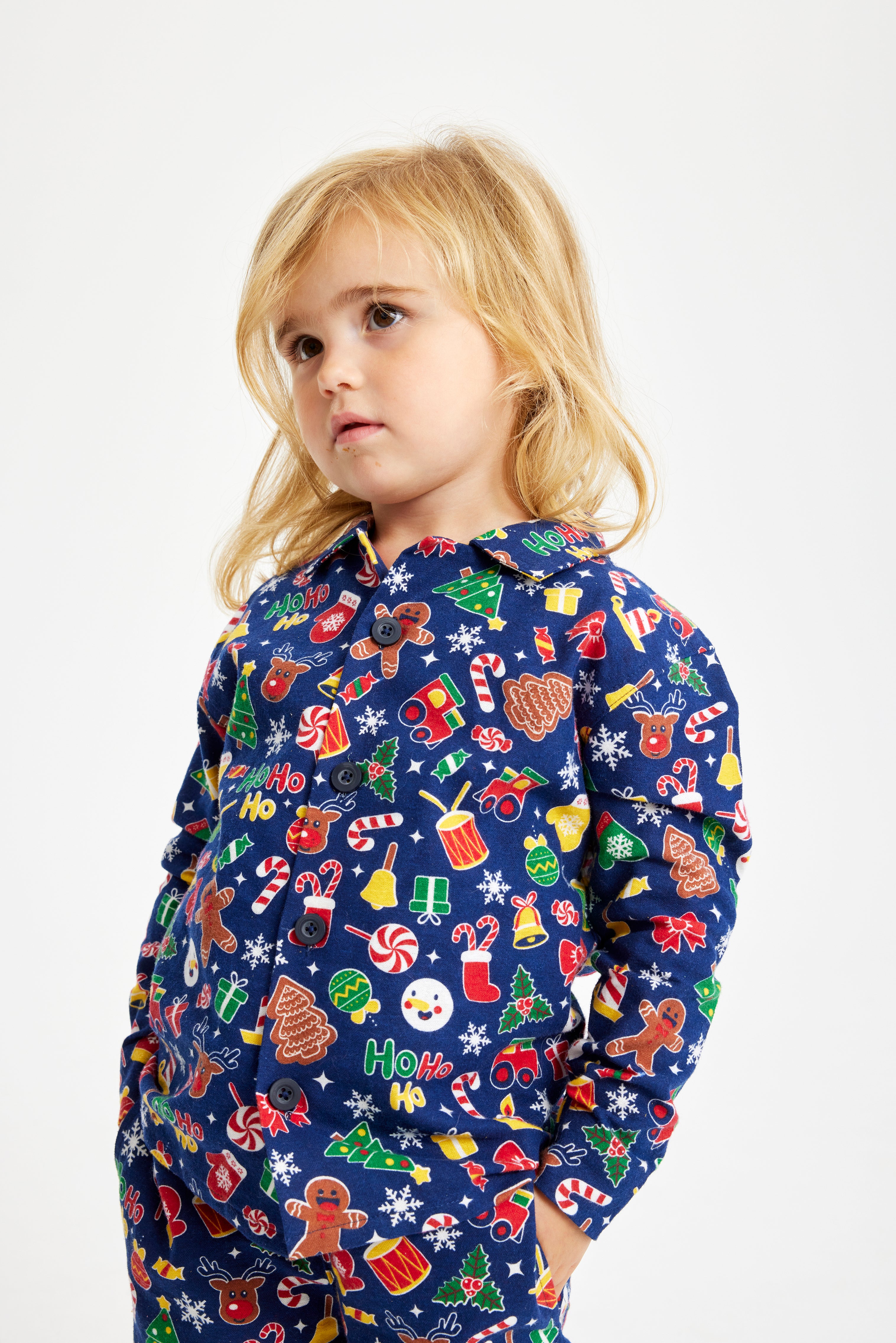 Et barn med en julepyjamas med juleslik, trommer, traktorer, kagemænd og juletræer.