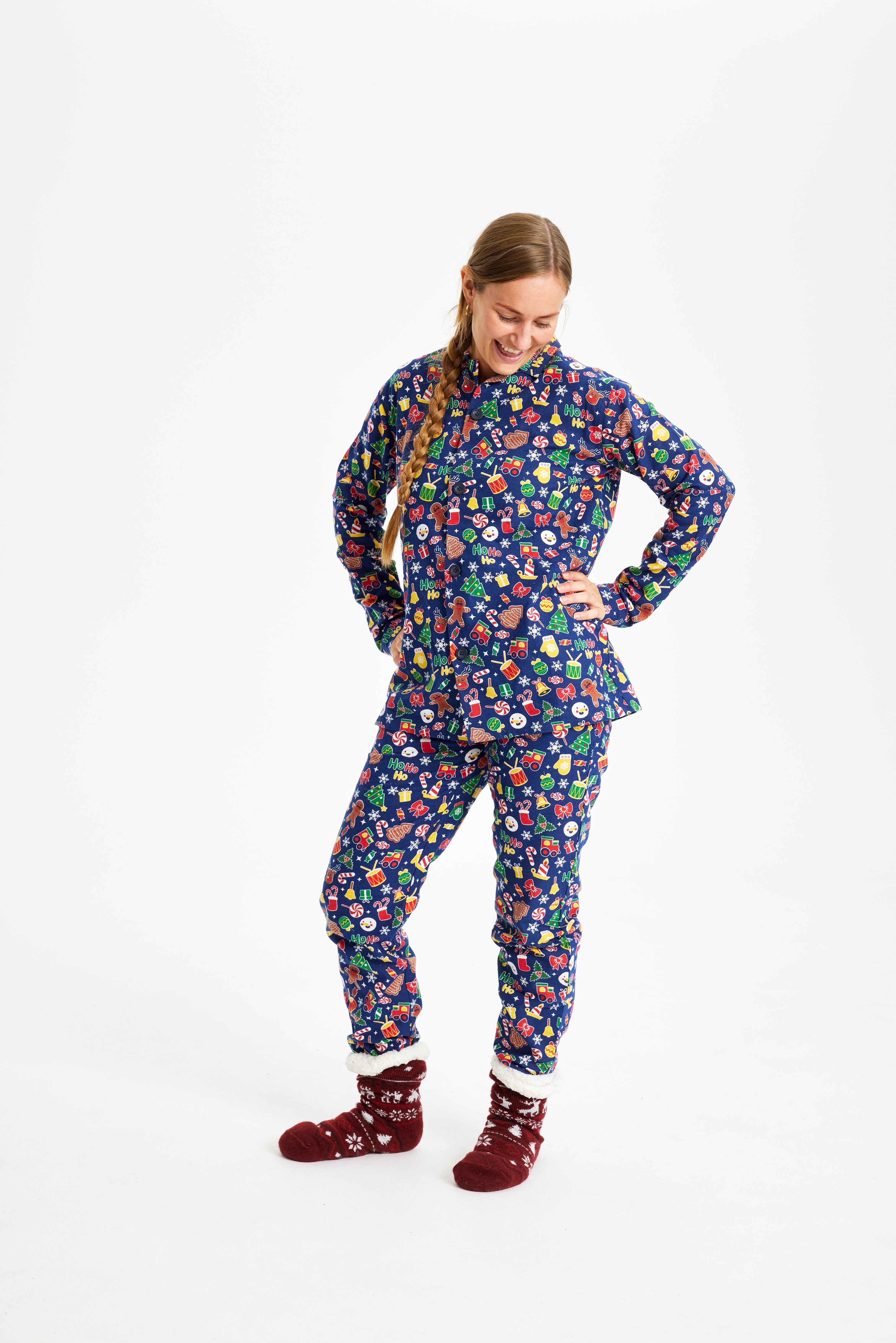 En poserende dame iført en mørkeblå julepyjamas med juletræer, julegodter, kagemænd og trommer.