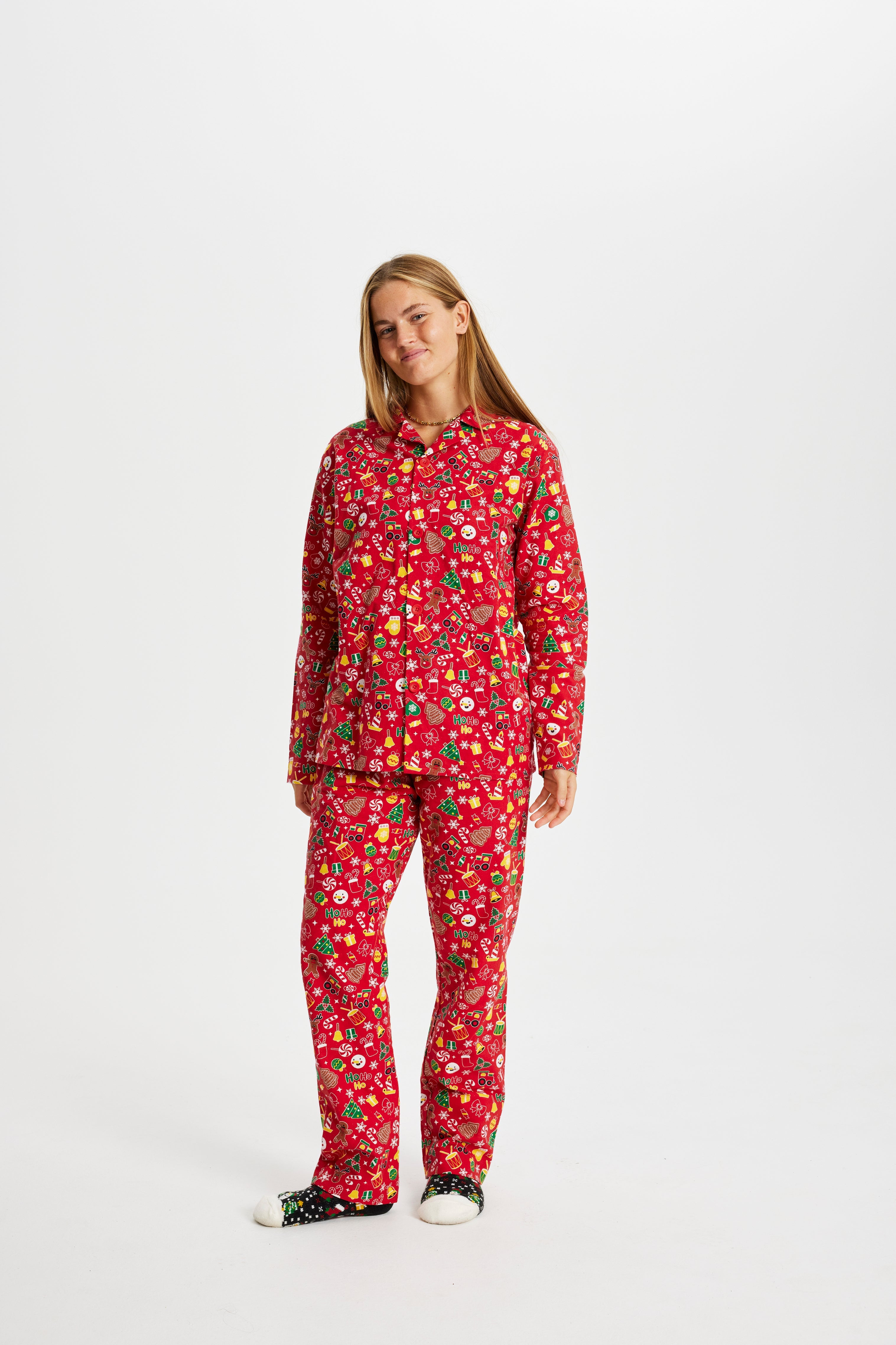 En smilende dame iført en rød julepyjamas med juletræer, vanter og klokker på.