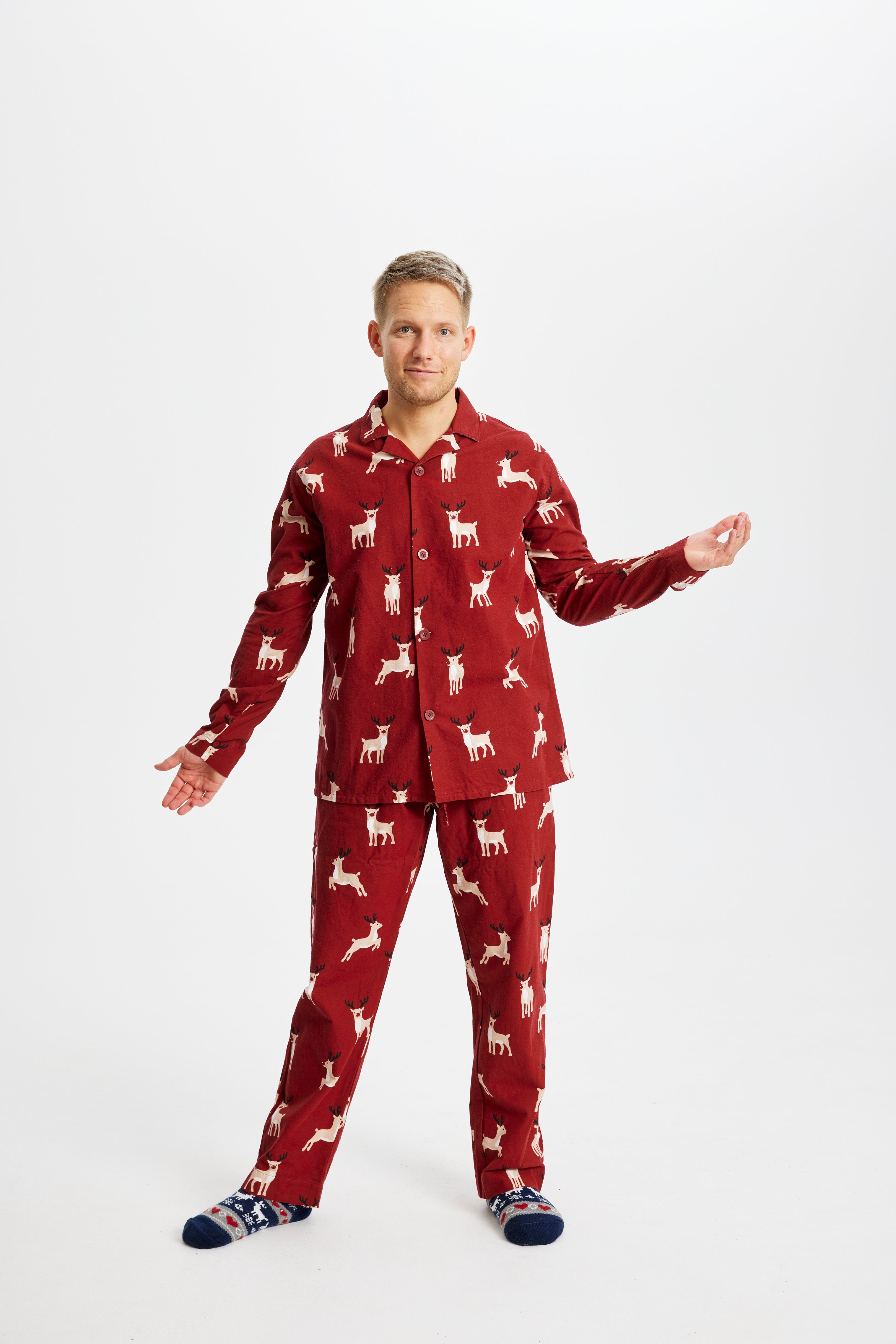 En mand med hænderne til siden poserer i sit røde pyjamassæt med rensdyr.
