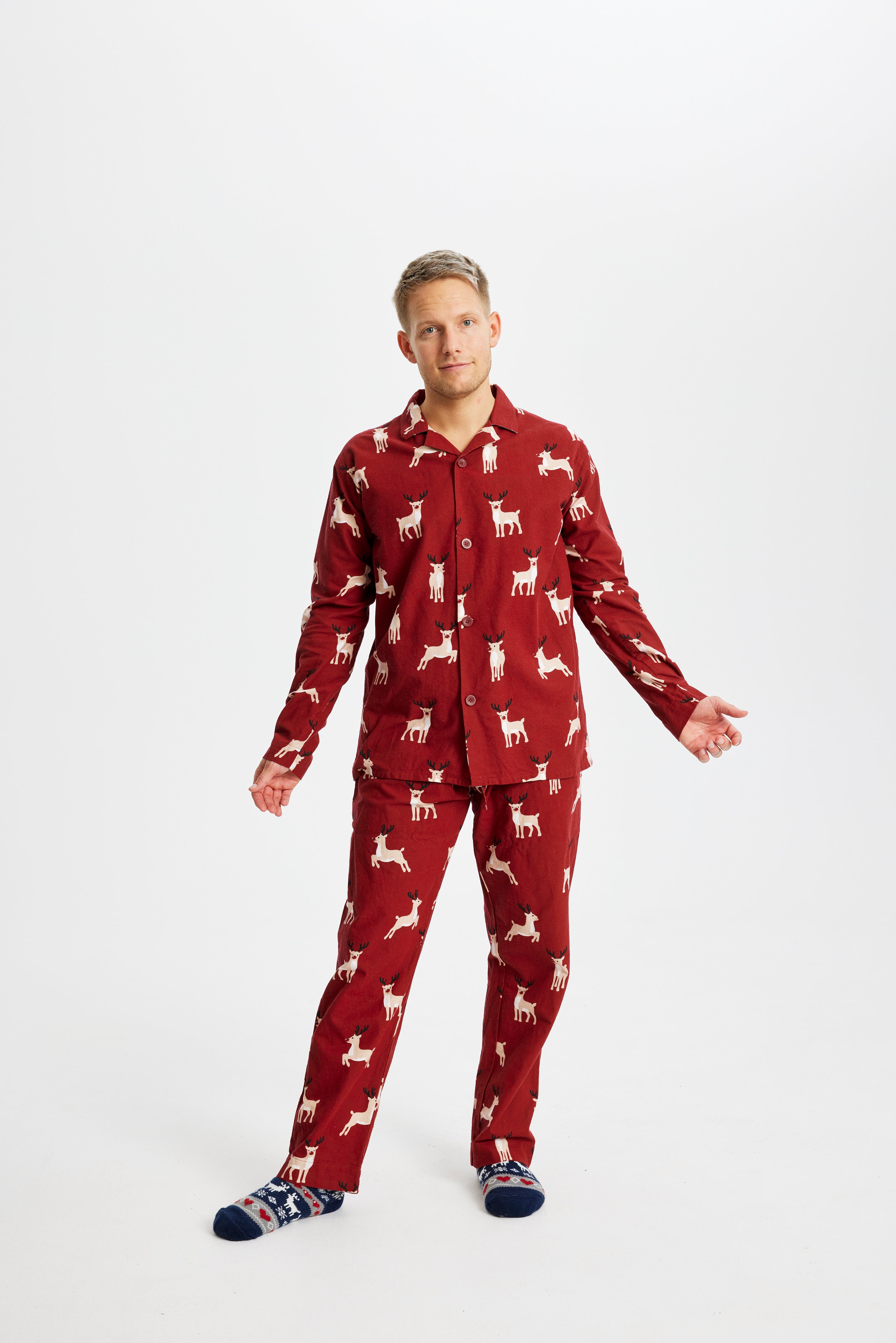 En mand poserer i sit røde pyjamassæt med rensdyr på.