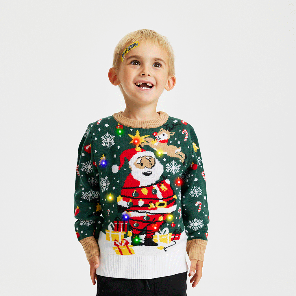 Et smilende barn iført en grøn julesweater med lys på.