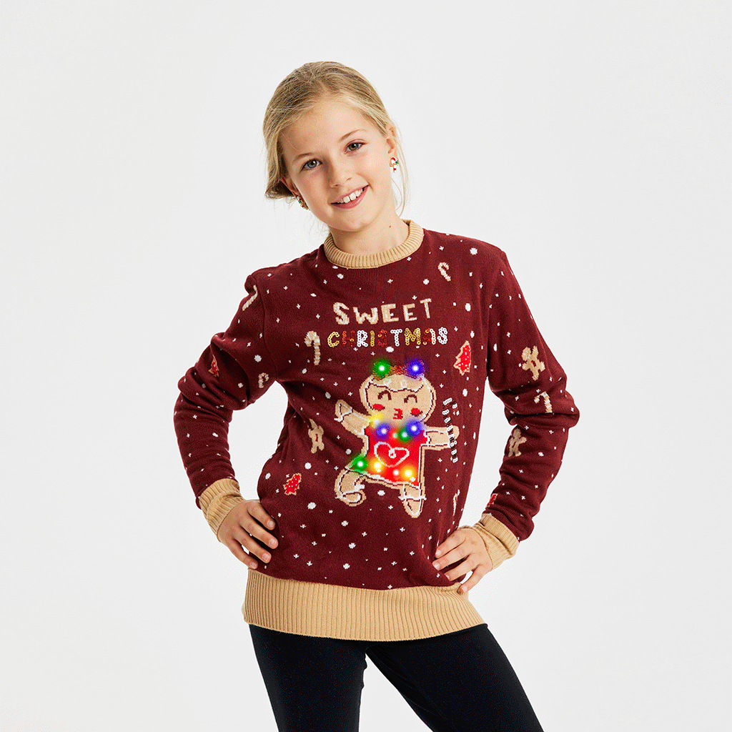 Et smilende barn iført en julesweater i rød med en kagekone, der danser og lyser.