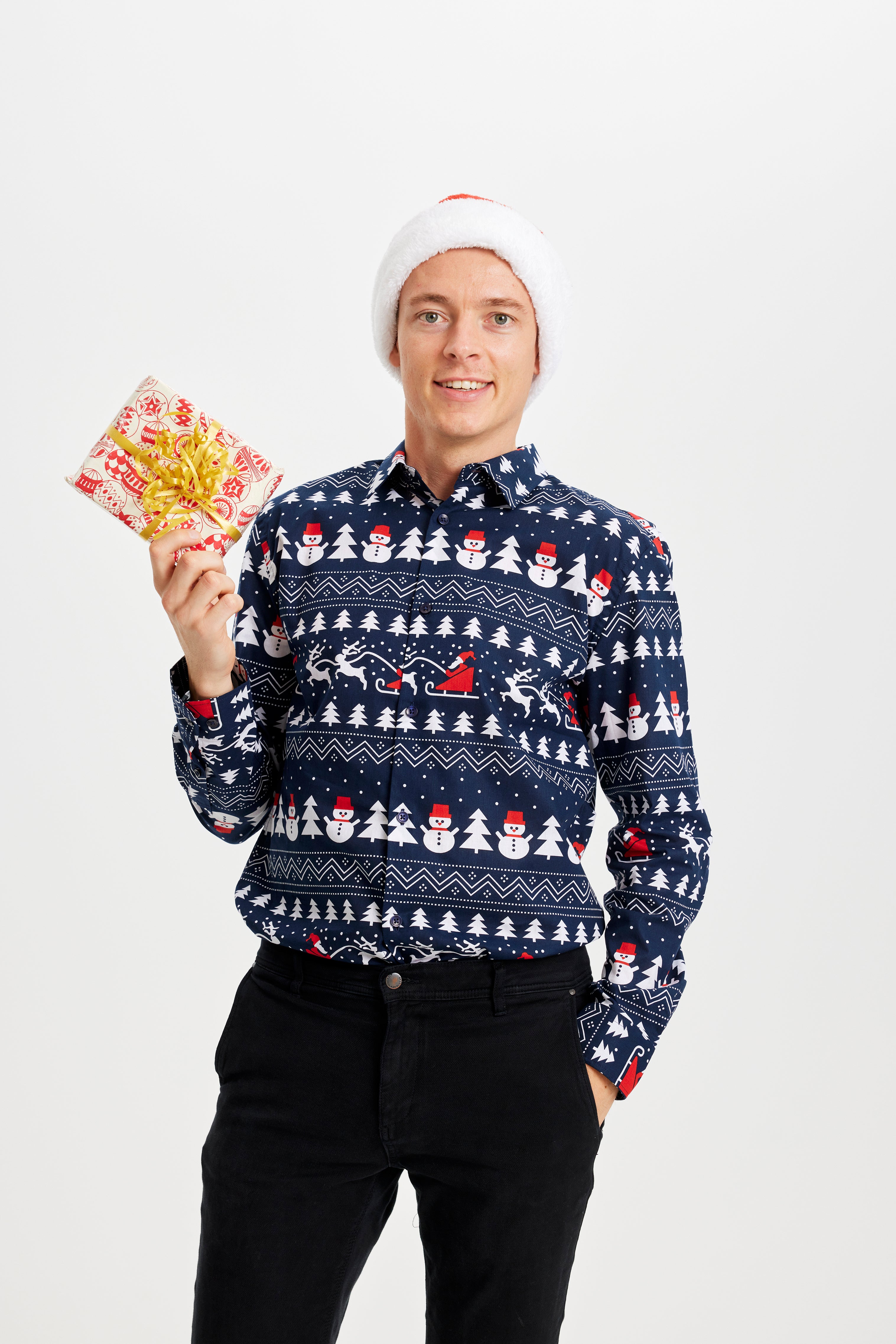 En smilende mand med en gave i hånden og er iført en blå juleskjorte.