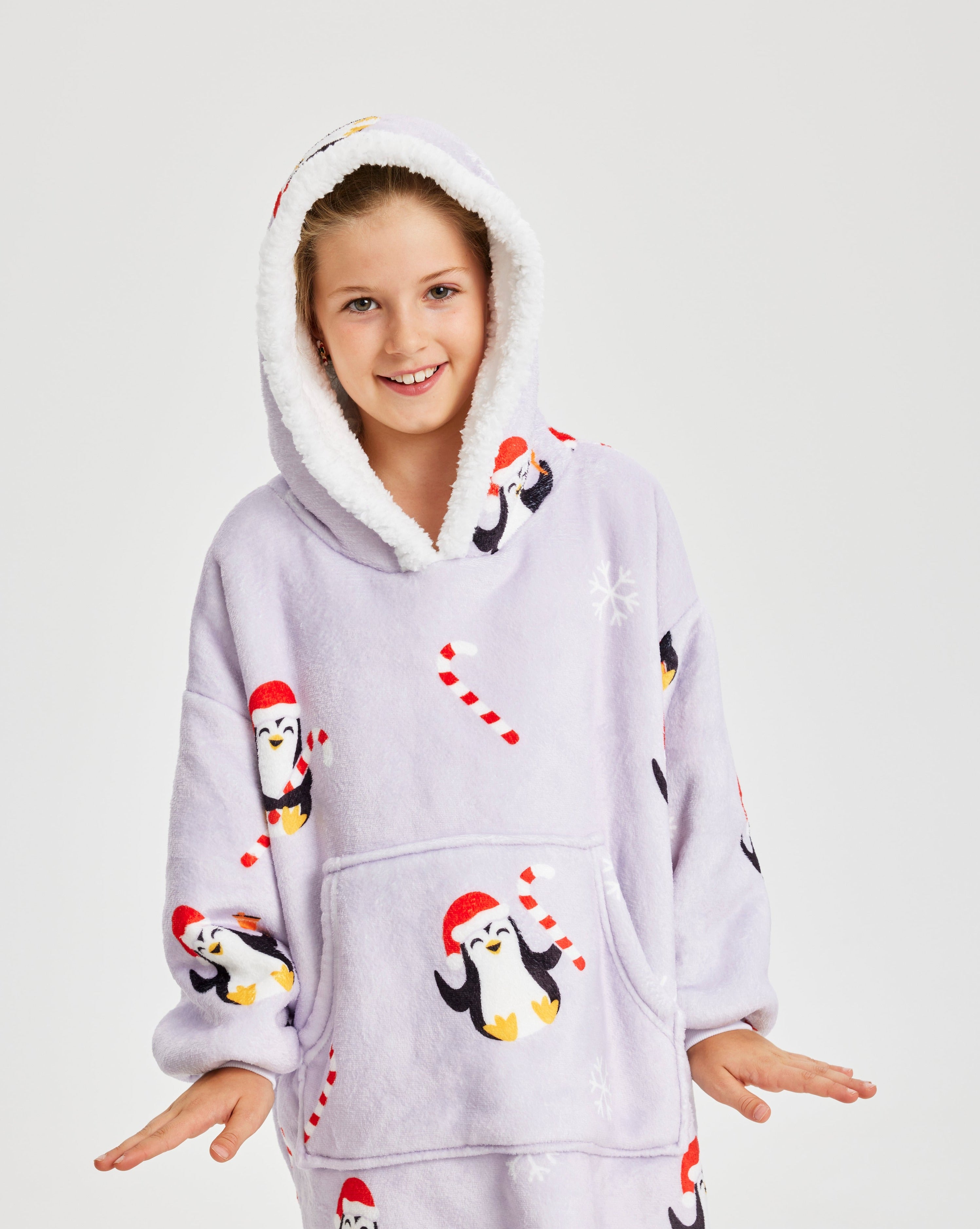 Et smilende barn iført en julehoodie med pingviner på.