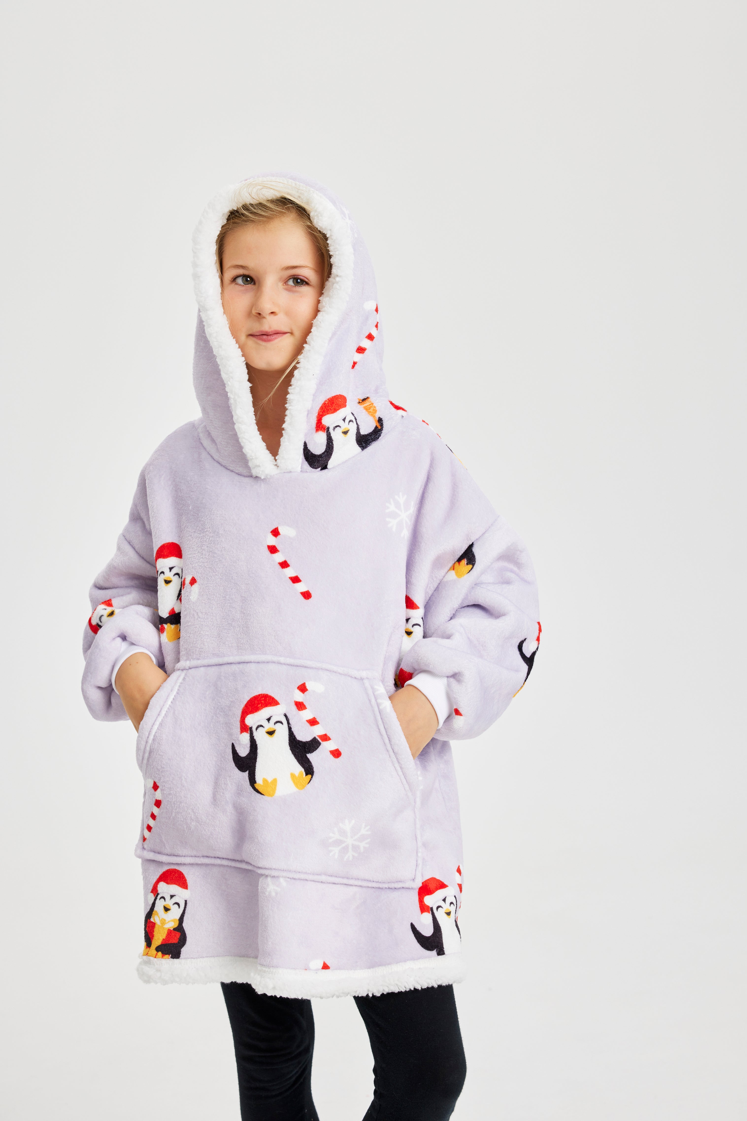 Et barn poserer i en julehoodie med sukkerstokke og pingviner på.