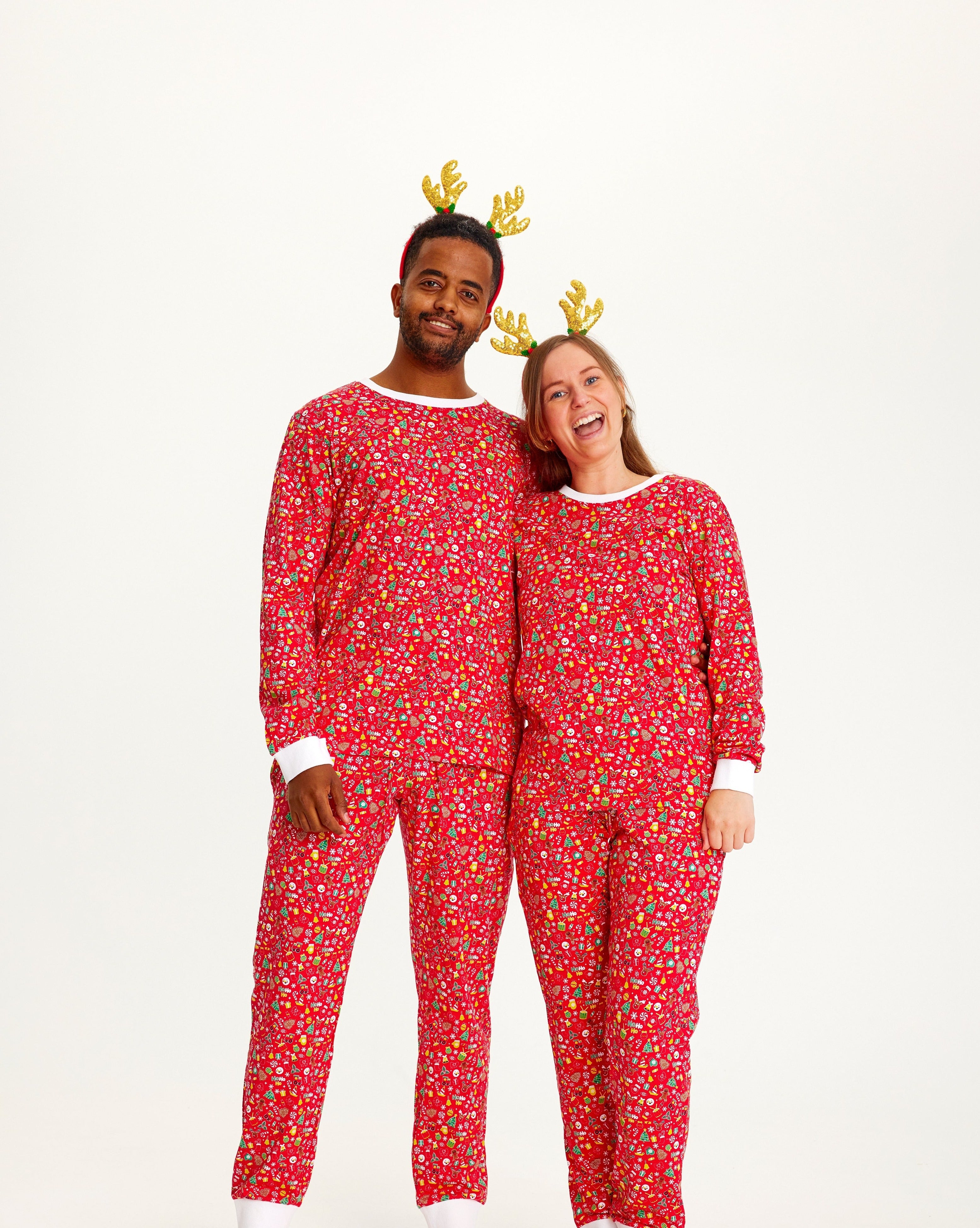 En mand og en kvinde poserer med rensdyrgevir og er iført en rød julepyjamas.