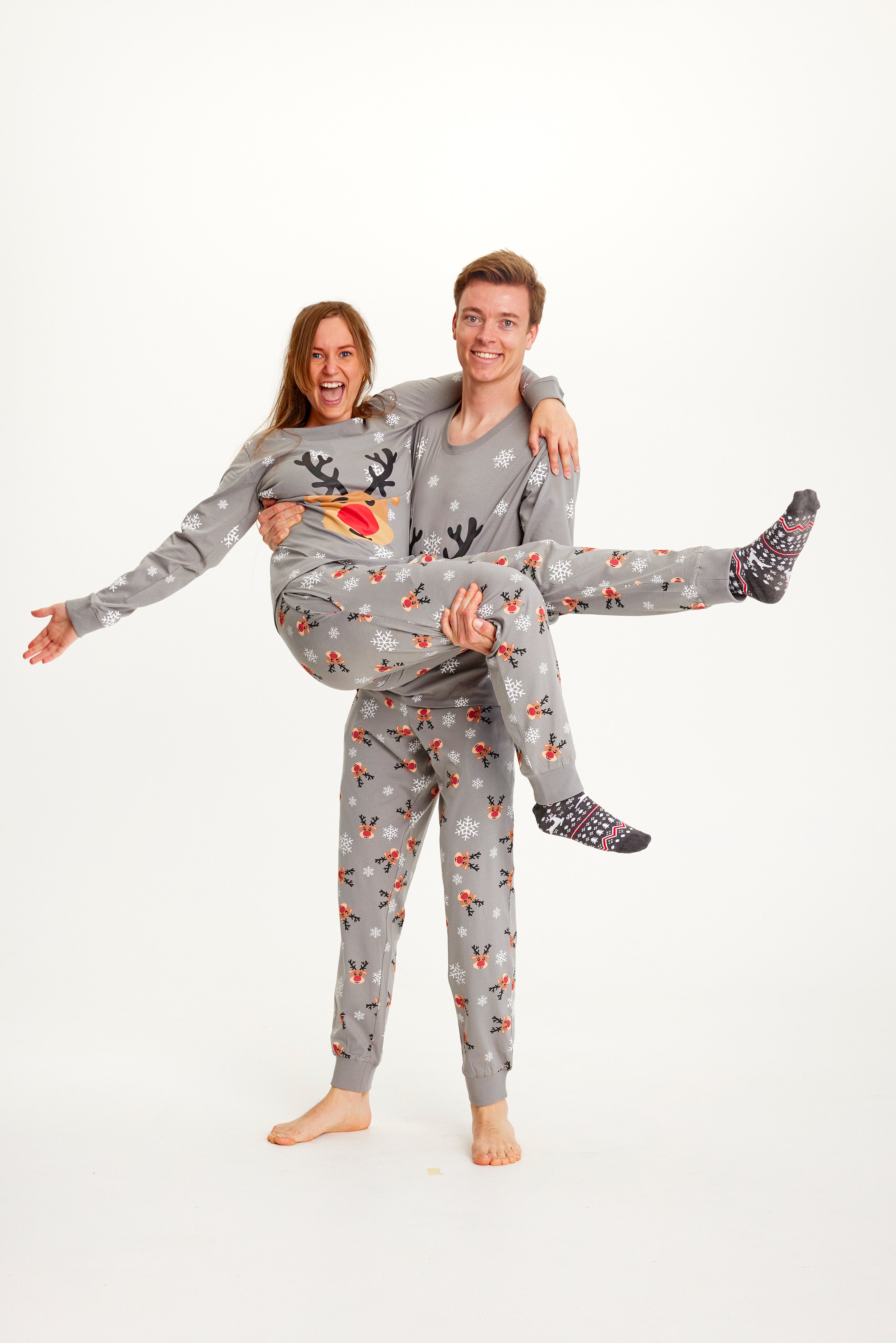 En dame og en mand poserer sammen iført grå julepyjamas med Rudolf på.
