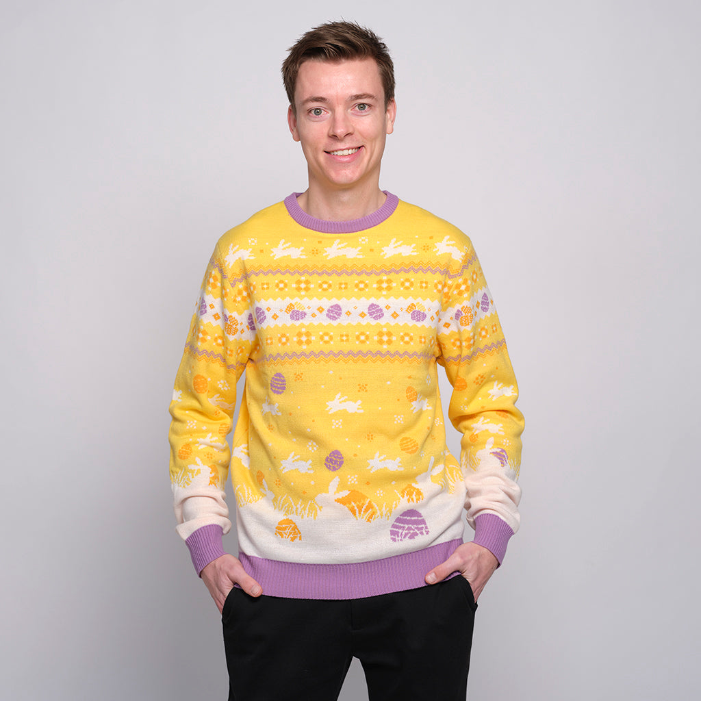 En smilende mand poserer i en gul påskesweater med påskeharer på.